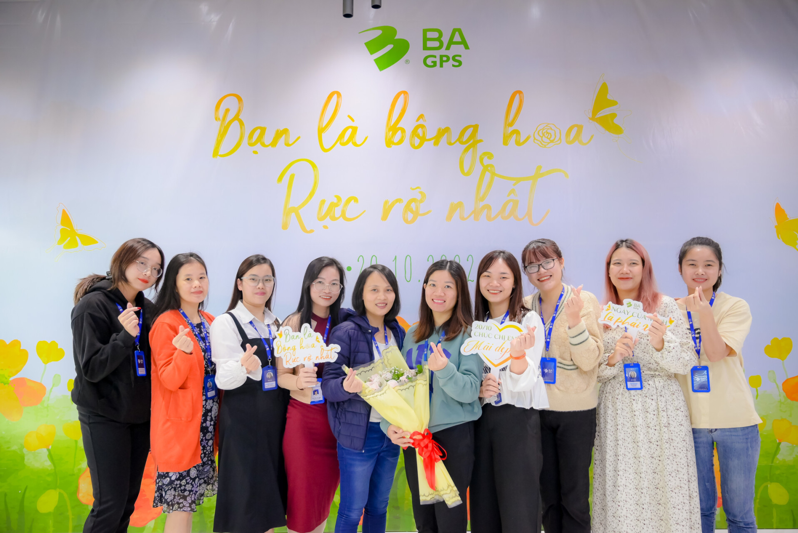 chị em các phòng ban tại VPHN xúng xính váy áo dưới backdrop "Bạn là bông hoa rực rỡ nhất"