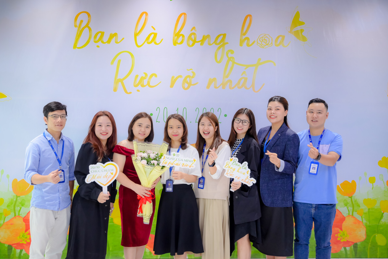 chị em các phòng ban tại VPHN xúng xính váy áo dưới backdrop "Bạn là bông hoa rực rỡ nhất"